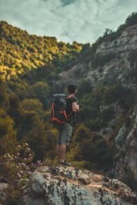 A man with a backpack stands on a rock, admiring the lush mountain landscape in Algeria.